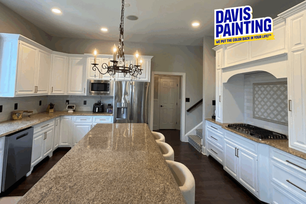 A modern kitchen with white cabinets, stainless steel appliances, granite countertops, a large island with chairs, a chandelier, and a "Davis Painting" logo in the top right corner.