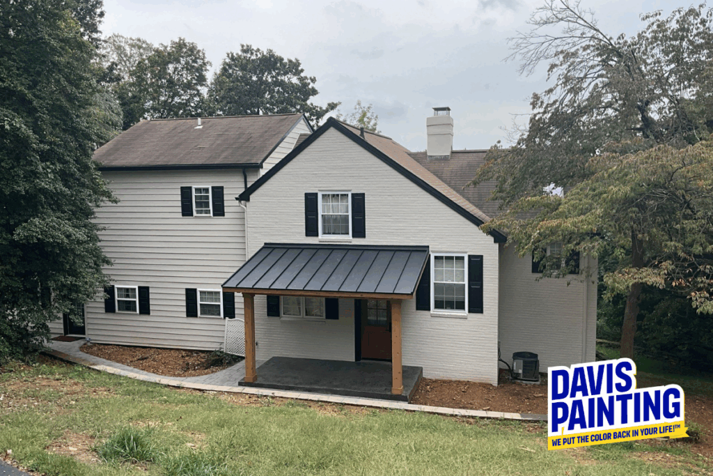 A two-story house with white brick and light gray siding, a black metal awning over the entrance, and a wooden front door. Trees surround the house. “Davis Painting” logo appears in the bottom right corner.