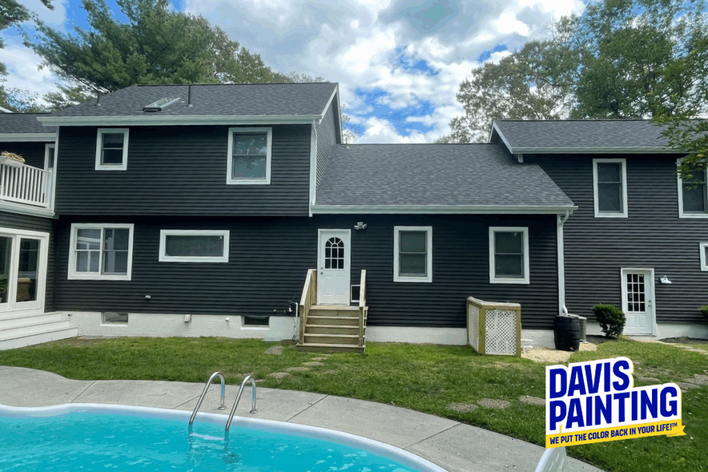 A dark gray two-story house with white trim, a small back porch with steps, and a swimming pool in the foreground. The Davis Painting logo is in the bottom right corner.