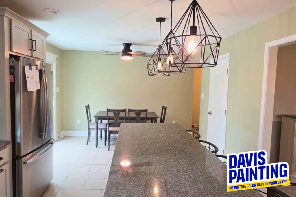 Modern kitchen with granite island, stainless steel appliances, pendant lights, and a dining table near a beige wall. “Davis Painting” logo is in the lower right corner.