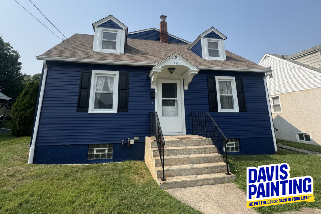 A blue house with white trim and black shutters, featuring a small front porch with steps. The lawn is green, and a “Davis Painting” logo appears in the bottom right corner.