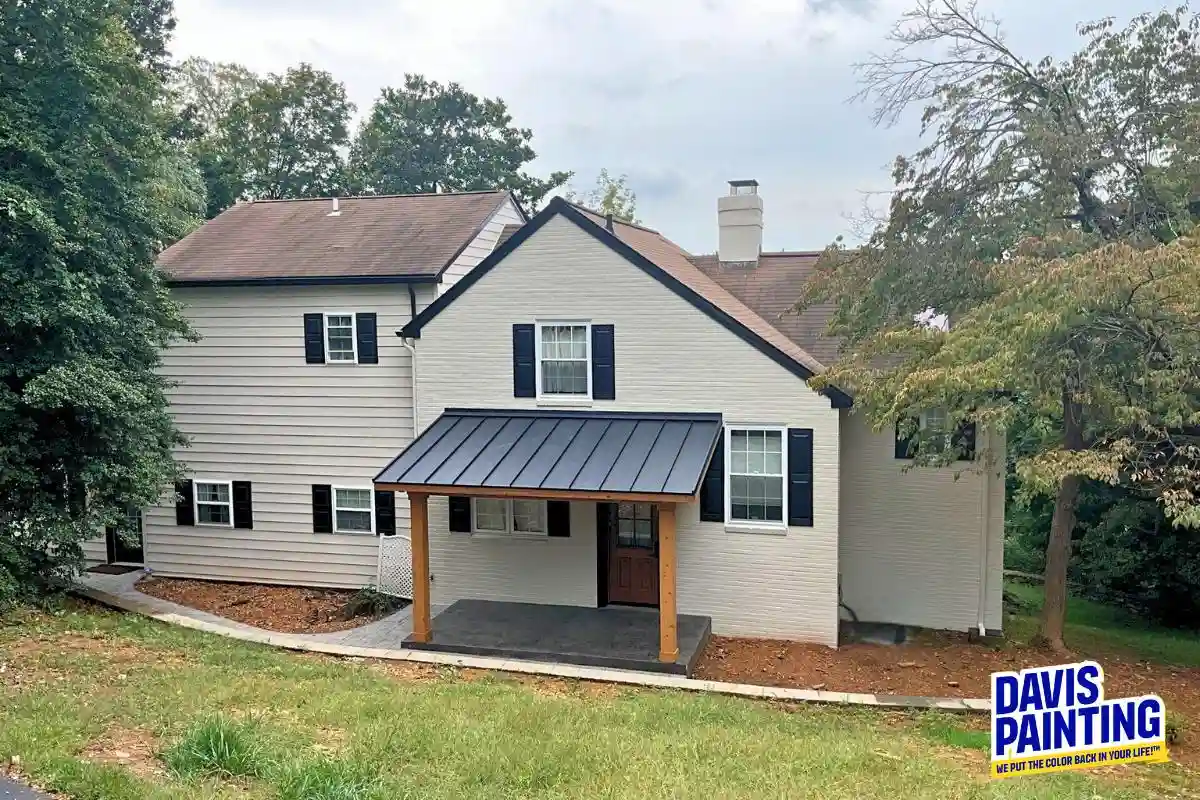 A two-story house with white brick and gray siding, black shutters, and a covered front porch. A Davis Painting sign is on the grass in the lower right corner. Limewashing PA Homes