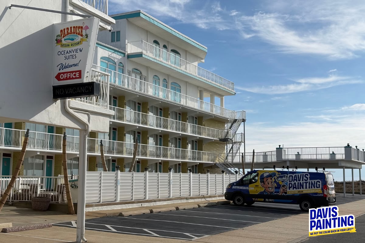 A multi-story hotel with balconies and an “Oceanview Suites” sign reading “No Vacancy.” A Davis Painting van, belonging to a leading Commercial Painting Contractor, is parked in front. Blue sky and some outdoor furniture are visible.